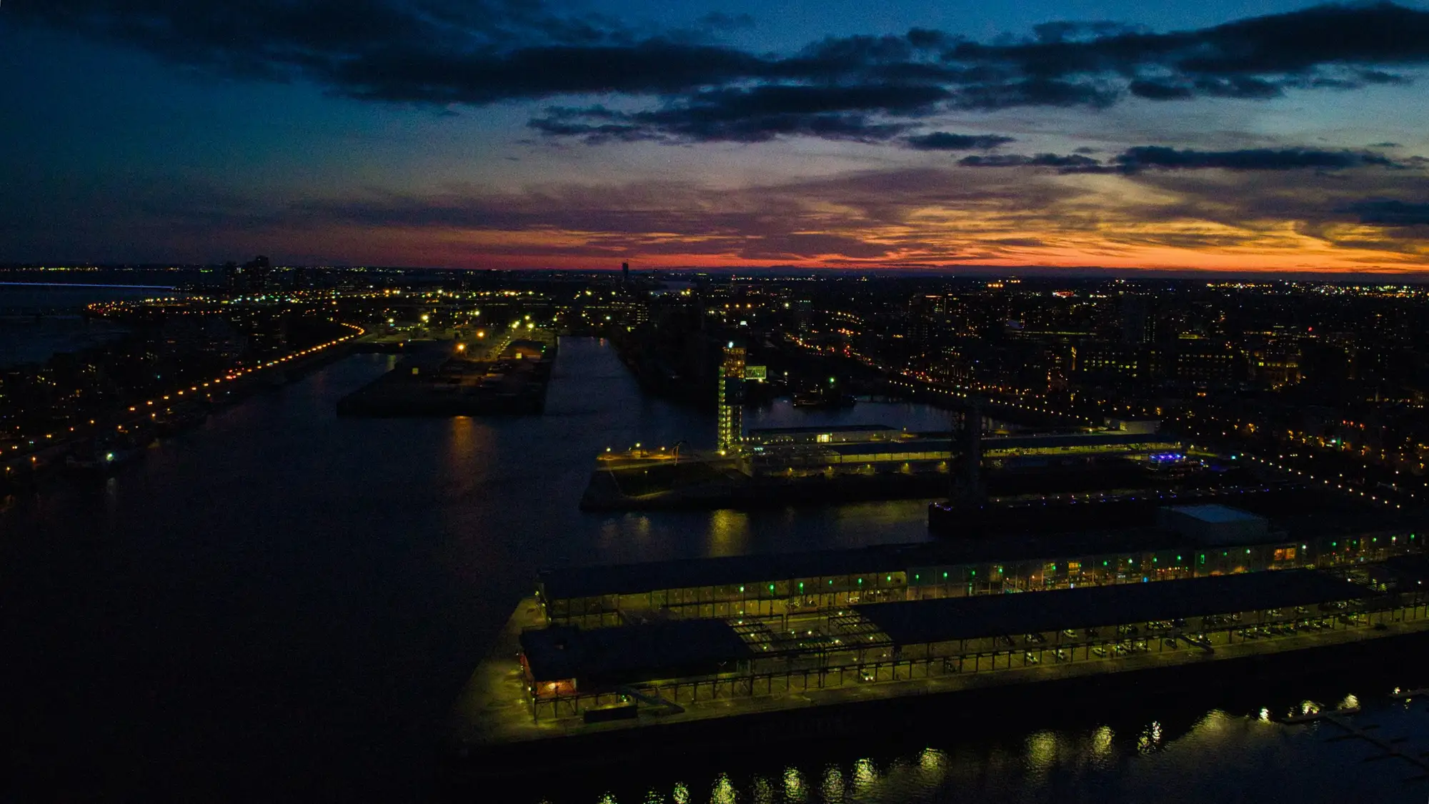 A city and harbour at dusk, lit by its infrastructure