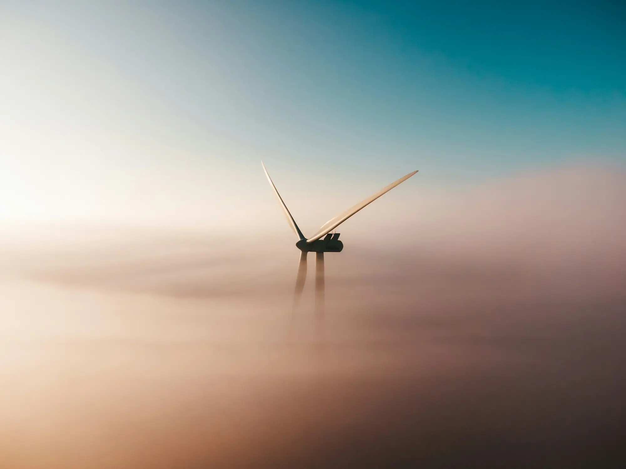 A single wind turbine emerging from fog at sunrise