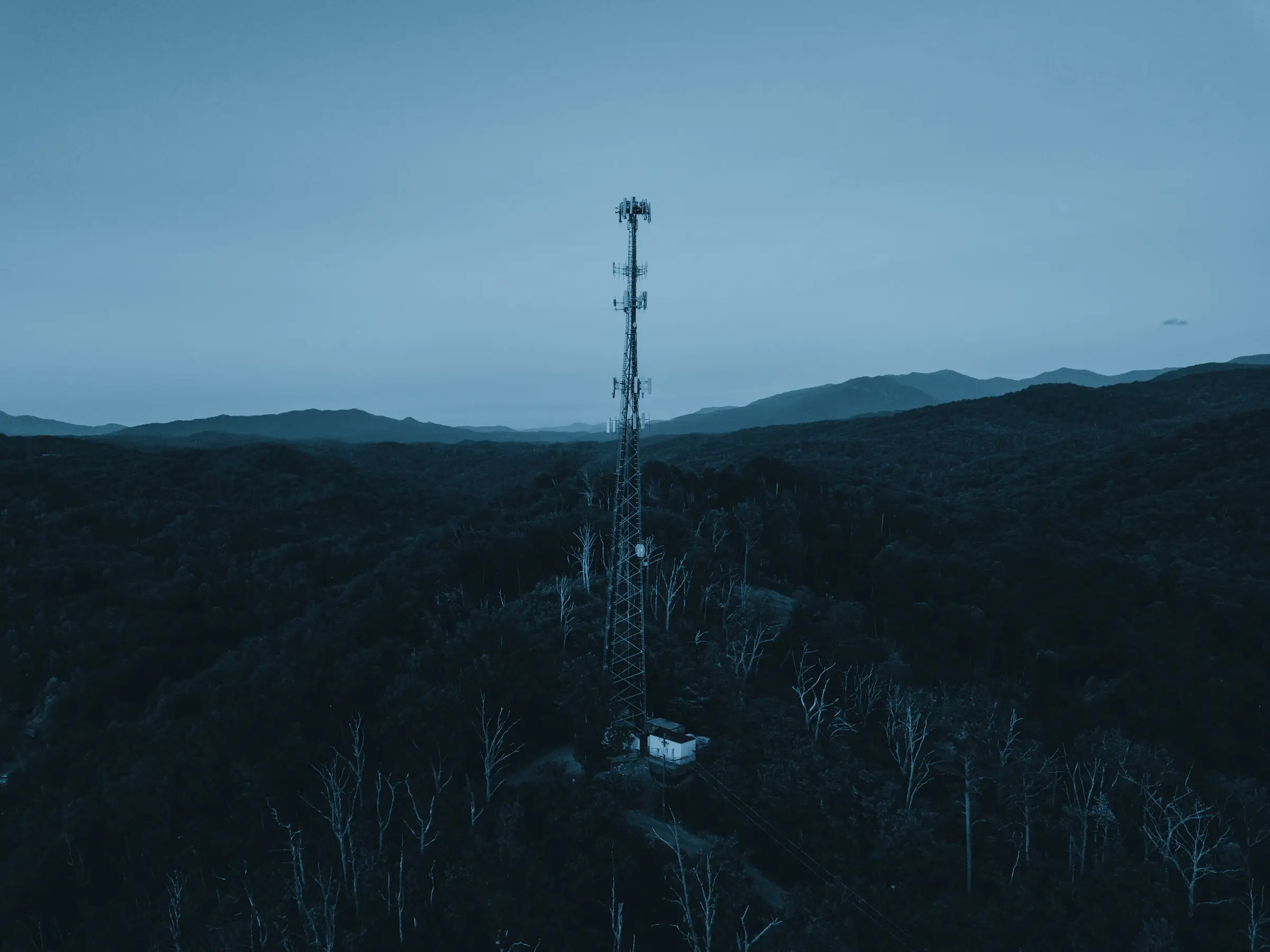 A communications tower on a forested ridge at dusk